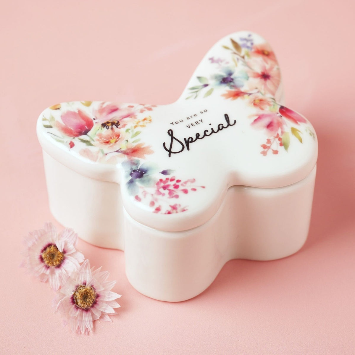 White glass butterfly-shaped trinket box with watercolour floral print, a bee detail, and "You are so VERY Special" script on the lid, plain white base, pink background.