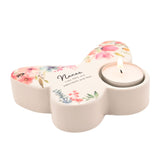 White glass butterfly-shaped tealight candle holder with pink, coral and blue floral design, a lit tealight in one wing, and "Nanas, Like YOU, are PRECIOUS and few" text at centre.