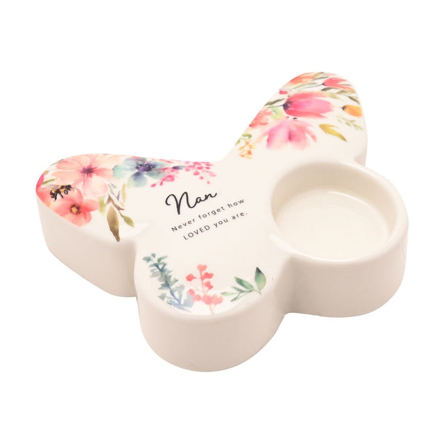 White butterfly-shaped glass tealight candle holder with pink, coral and blue floral design, a small bee, and "Nan" script, single tealight cup in one wing, on a plain white background.