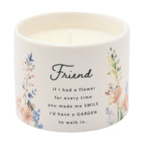 Round ceramic scented candle in off-white with watercolour wildflower prints and "Friend" script with sentimental verse, white wick visible, shown on a plain background.