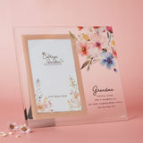 Clear glass photo frame with peach-bordered 6x4in opening, floral and bee print, and "Grandma" verse in script, set against a pink background.