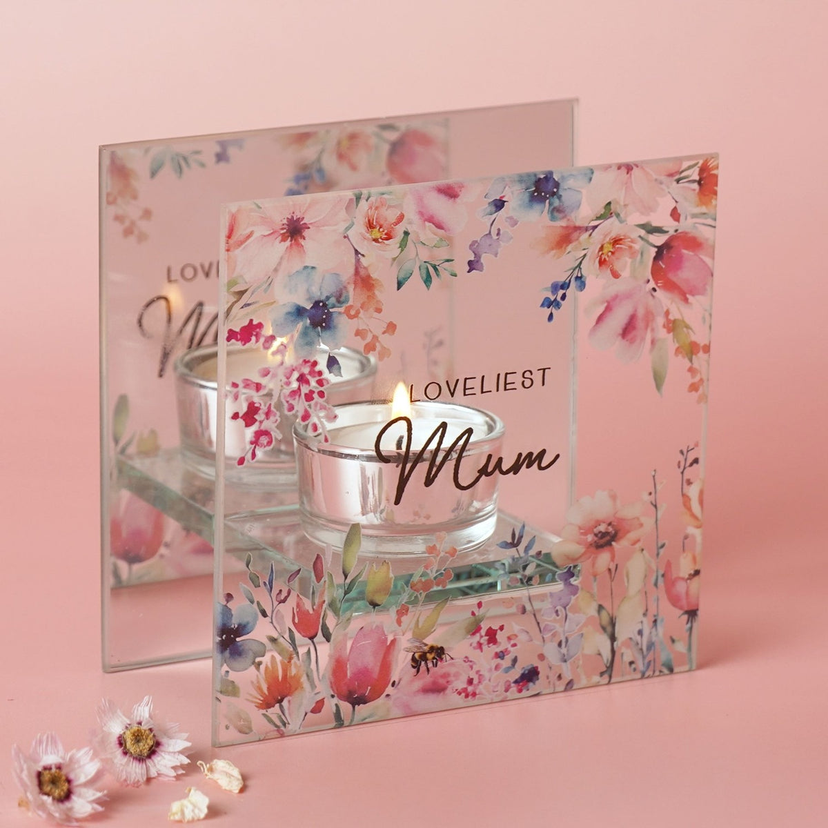 Square glass tealight candle holder with "Loveliest Mum" script, watercolour floral and bumblebee design, mirrored back panel, lit candle, on a pink background.