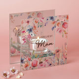 Square glass tealight candle holder with "Loveliest Mum" script, watercolour floral and bumblebee design, mirrored back panel, lit candle, on a pink background.