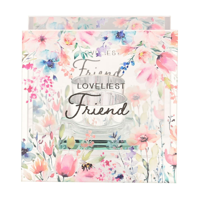 Square clear glass tealight holder printed with Loveliest Friend in script, framed by watercolour wildflowers and a bee, with a round glass cup resting on a narrow ledge.
