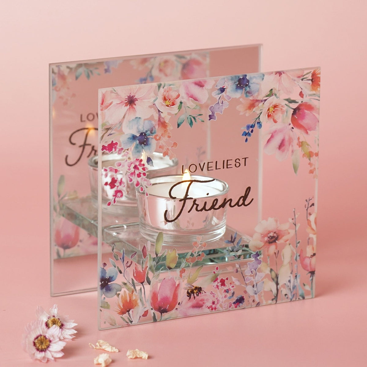 Square glass tealight holder with Loveliest Friend script, watercolour floral and bee design, lit candle inside, set against a pink background.