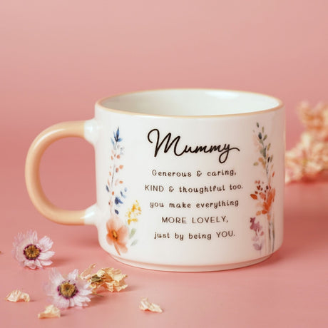 White stoneware mug with peach handle, featuring "Mummy" script, a verse, and watercolour wildflowers, set against a pink background with dried flowers.