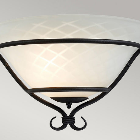 The Torchiere 1 Light Wall Uplighter boasts Gothic elegance, showcasing an etched opal glass shade with a diamond pattern. Housed in a sleek black metal frame with graceful curves, it casts a soft, warm glow against a simple neutral grey background.