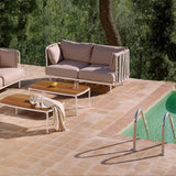 Teja Rope 2 Seater Garden Sofa with white aluminium frame, vertical rope-wrapped arms, and beige cushions, shown on a poolside terrace with a coffee table and footstool.