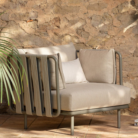 Teja Rope Garden Armchair with beige cushions, anthracite aluminium frame and woven rope side panels, shown outdoors against a stone wall with a palm plant.