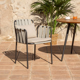 Teja rope garden dining armchair with anthracite aluminium frame, woven rope back and sides, and beige seat and back cushions, shown on a sunlit terrace beside a round wood-topped table.