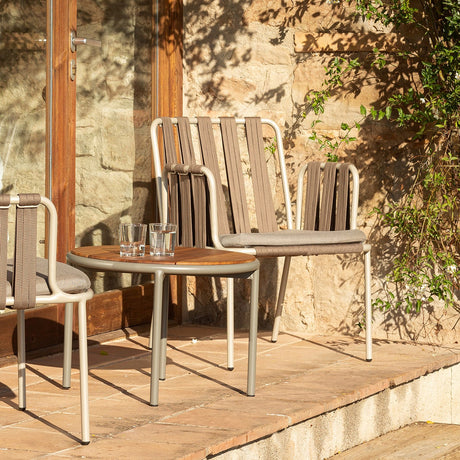 Teja Rope Garden Lounge Chair with woven beige rope back and arms, grey seat cushion and aluminium frame, shown with a matching chair and side table on a sunlit outdoor terrace.