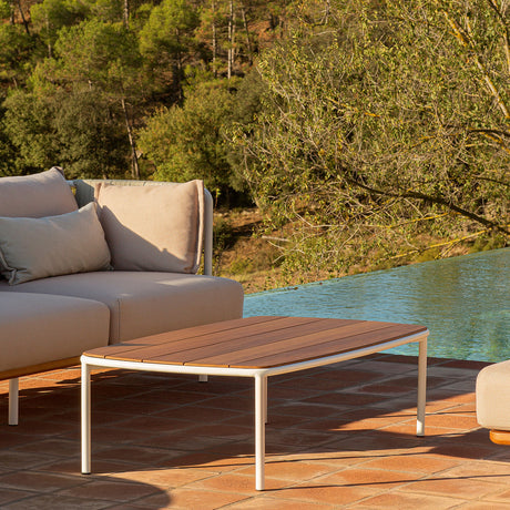 Teja Aluminium Outdoor Coffee Table, 120 x 70cm, with wood-effect slatted top and white rounded frame, shown poolside beside a grey outdoor sofa.