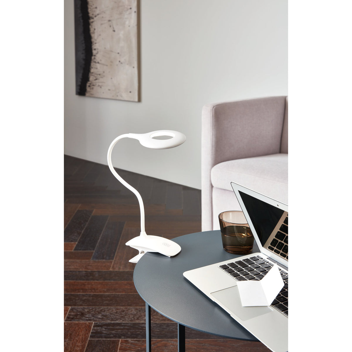 Telarne Clamp Lamp 42cm in white plastic with a flexible gooseneck and ring-shaped LED head, clipped to a side table beside a laptop in a living room setting.
