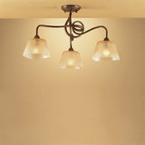 Mantra Tentacle 3 light semi-flush ceiling light with rustic gold intertwined metal arms and frosted amber glass shades, mounted to a warm-toned ceiling.