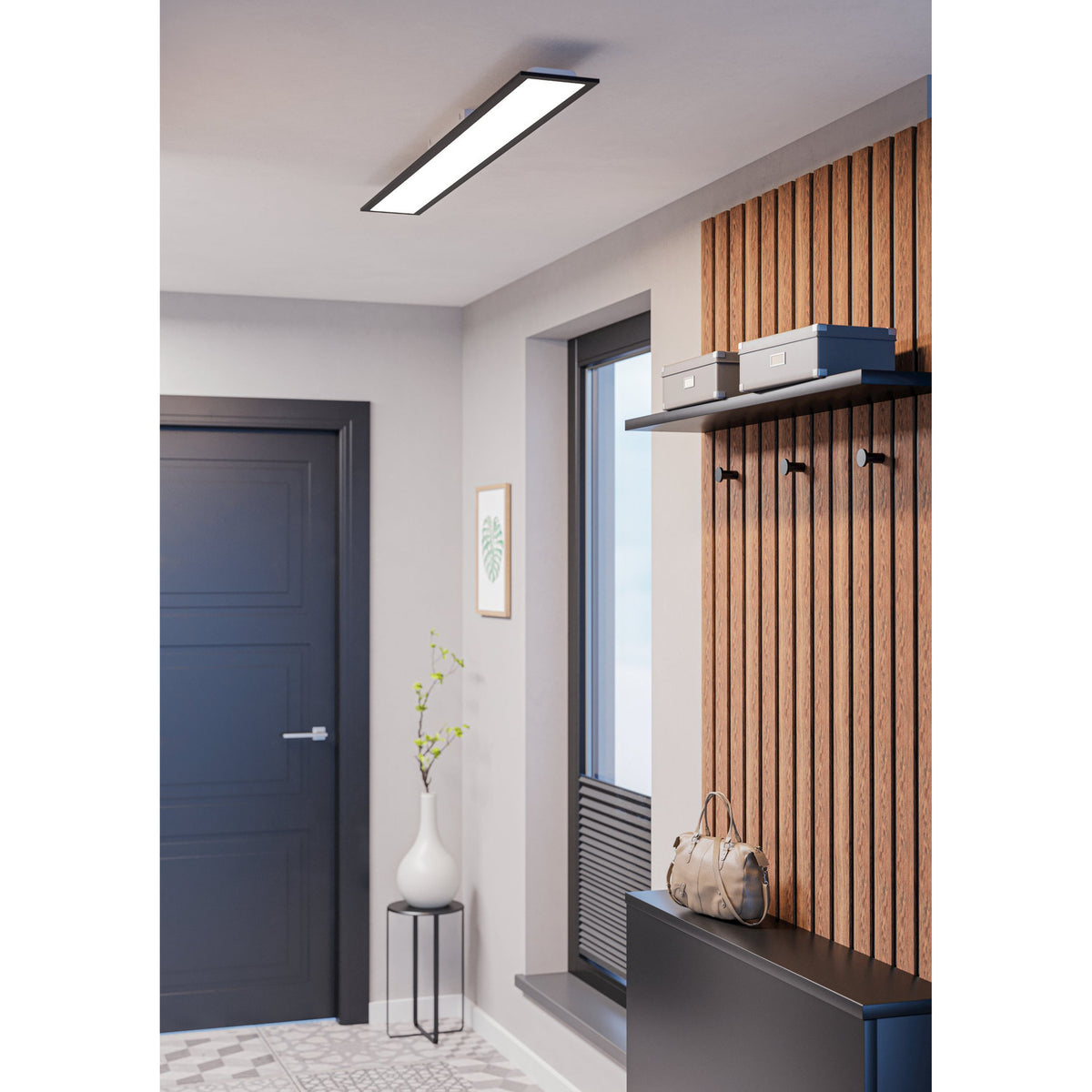 Tesvelle LED Panel Light, a slim rectangular ceiling fixture with black steel frame and white diffuser, shown illuminated above a hallway with wood slat wall and dark door.