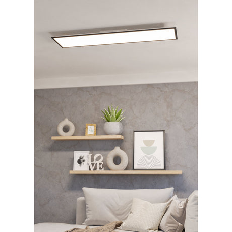 Tesvelle rectangular LED ceiling panel light with black steel frame and white diffuser, mounted flush on a living room ceiling above styled wall shelves and a sofa.