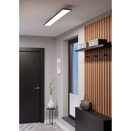 Tesvelle slim rectangular LED ceiling panel with black steel frame and white diffuser, shown lit above a hallway with wood-slat wall, shelf and dark door.