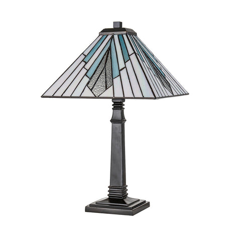 The Alderley 1 Light Large Table Lamp in vintage bronze features a stained glass shade adorned with geometric patterns in white, blue, and gray. It boasts a dark, angular base atop a square platform, reminiscent of Tiffany-style lighting from the Arts and Crafts architectural era.