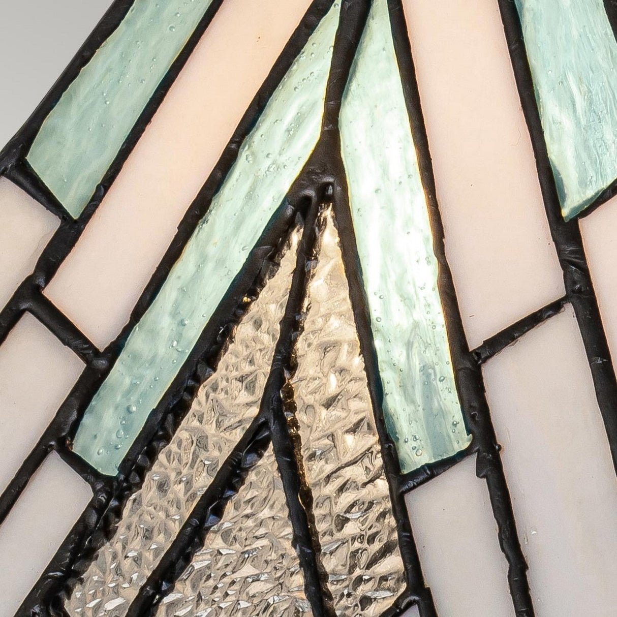 Close-up of the Alderley 1 Light Medium Table Lamp in Vintage Bronze, showcasing a design reminiscent of a stained glass window with Tiffany-style inspiration. The lamp features varied geometric patterns crafted from both textured and smooth glass pieces in shades of white, teal, and clear, all outlined with dark edges.