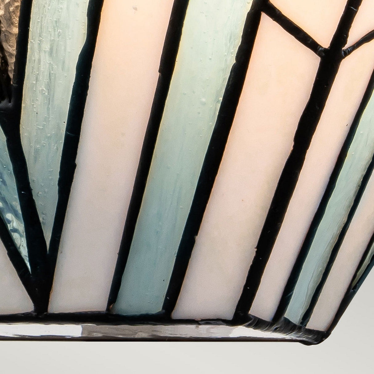 Close-up of a stained glass lampshade showcasing geometric patterns inspired by Art Deco, with cream and light blue panels divided by black lead lines. It perfectly complements the Alderley 2 Light Wall Uplighter - Vintage Bronze for a timeless touch.