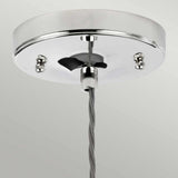 A close-up showcases a polished nickel metallic ceiling canopy secured with two screws, from which a single gray fabric-covered cord descends. The Tiber 1 Light Pendant - Polished Nickel/Clear Glass enhances the decor with its elegance, standing out against a soft gray background.