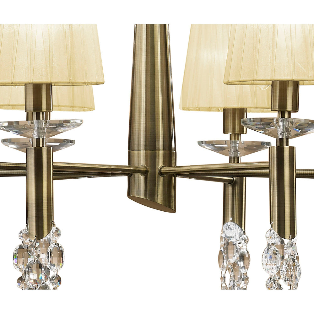 Close-up of Tiffany chandelier showing antique brass central column, curved arms, cream pleated shades, and faceted crystal droplets.
