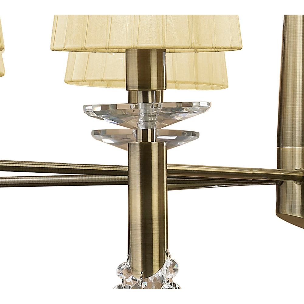 Close-up of Tiffany chandelier arm in antique brass with cream pleated fabric shades and faceted crystal accents above the tiered support.