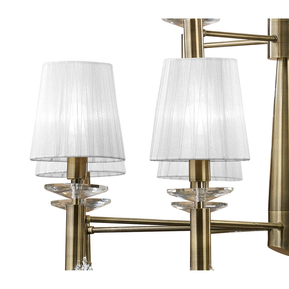Close-up of Tiffany chandelier arms in antique brass with pleated white fabric shades and faceted crystal droplets beneath each fitting.