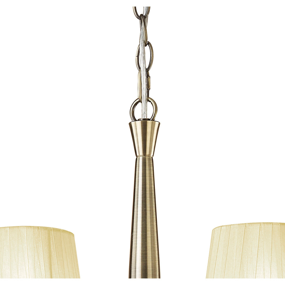 Close-up of the Tiffany chandelier's antique brass central column and chain suspension, with two cream pleated fabric shades visible below.