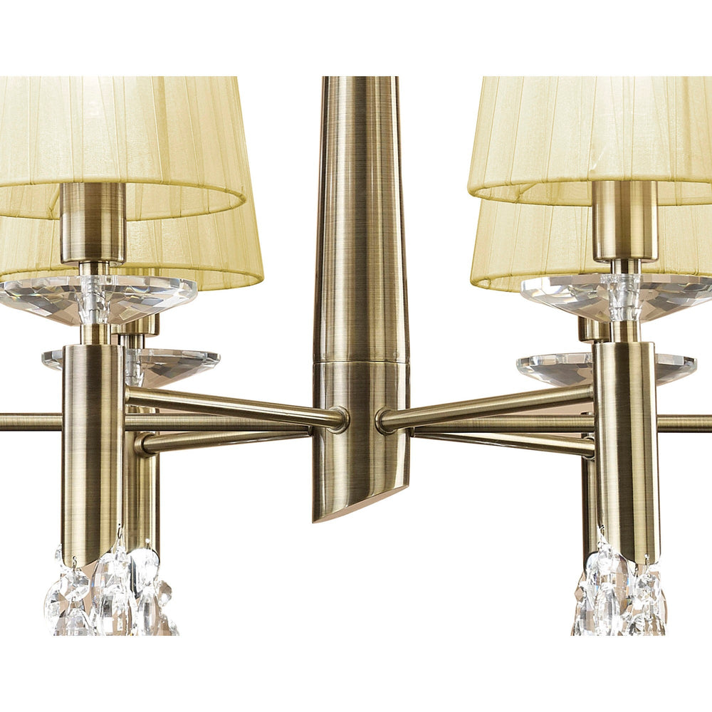 Close-up of the Tiffany 6 light chandelier showing the antique brass central column, arms, cream pleated shades, and faceted crystal accents.