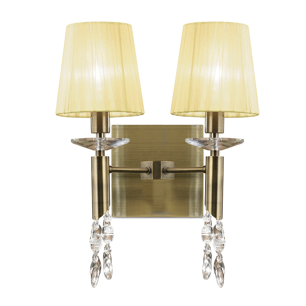 Tiffany 2 light wall fitting in antique brass with cream pleated fabric shades and hanging faceted crystal droplets on a white background.