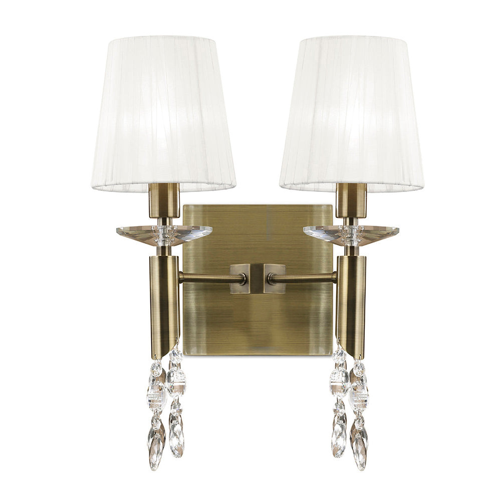 Tiffany 2 light wall light with antique brass backplate, twin arms, white pleated fabric shades and crystal droplets, on a white background.