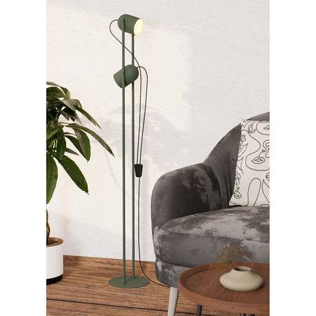 Tilston Floor Lamp in muted green steel with two cylindrical spot heads on slim twin rods and a round base, shown beside a grey sofa in a living room.