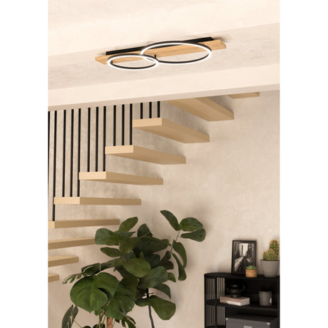 Timarne LED 2 Light Flush Ceiling Light in black and brown, featuring a wooden bar with two overlapping black ring shades, shown mounted above a staircase in a hallway setting.