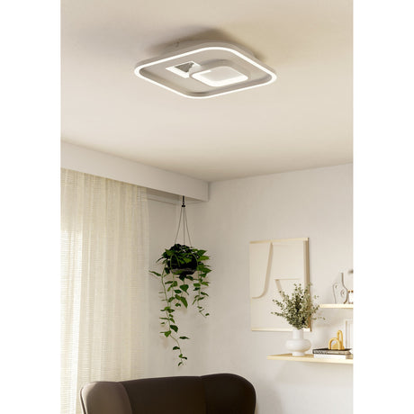 Tiriolo square LED ceiling panel light in white and silver with offset inner ring, mounted flush to the ceiling in a living room above a hanging plant and sofa.