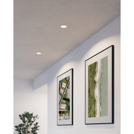 Tomelle Downlight in white aluminium recessed into a grey ceiling above a hallway, shown lighting two framed aerial landscape prints on a white wall.
