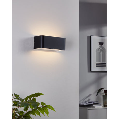 Tomessa LED Wall Light 20cm in black aluminium with white diffuser, mounted on a hallway wall casting warm uplight and downlight.