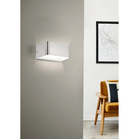 Tomessa LED Wall Light 20cm in satin nickel aluminium, mounted on a grey wall above a wooden armchair, casting warm white up-and-down light.