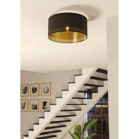 Tonvorne flush ceiling light in black fabric with brushed gold lining, mounted above a staircase, showing its drum shade with cut-out pattern and single E27 bulb.
