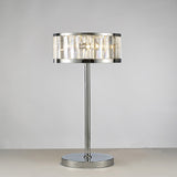 The Torre 3 Light Crystal Table Lamp features a polished chrome base and vertical clear glass panels, emitting a soft, warm glow against a light gray background.