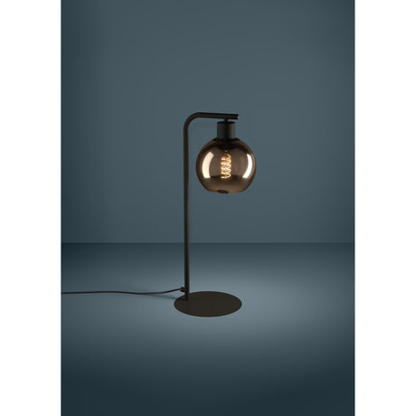 Trelbette Table Lamp in black steel with a round, mirrored copper-toned glass shade on a slim curved arm and flat base, shown lit against a dark background.