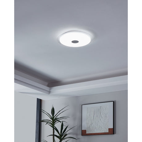 Trelmanne LED flush ceiling light in white and clear, round diffuser with chrome centre disc, shown illuminated on a grey ceiling in a hallway with coving.