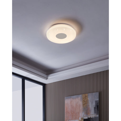 Trelmanne 56cm round LED flush ceiling light with white crystal-effect diffuser, clear outer ring and chrome centre disc, shown glowing warm white on a bedroom ceiling.