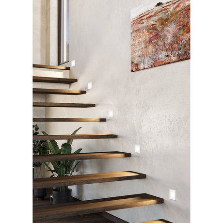 Trewellard LED Downlight 12 x 8cm in white, shown recessed into a staircase wall, illuminating wooden stair treads with a warm white glow.
