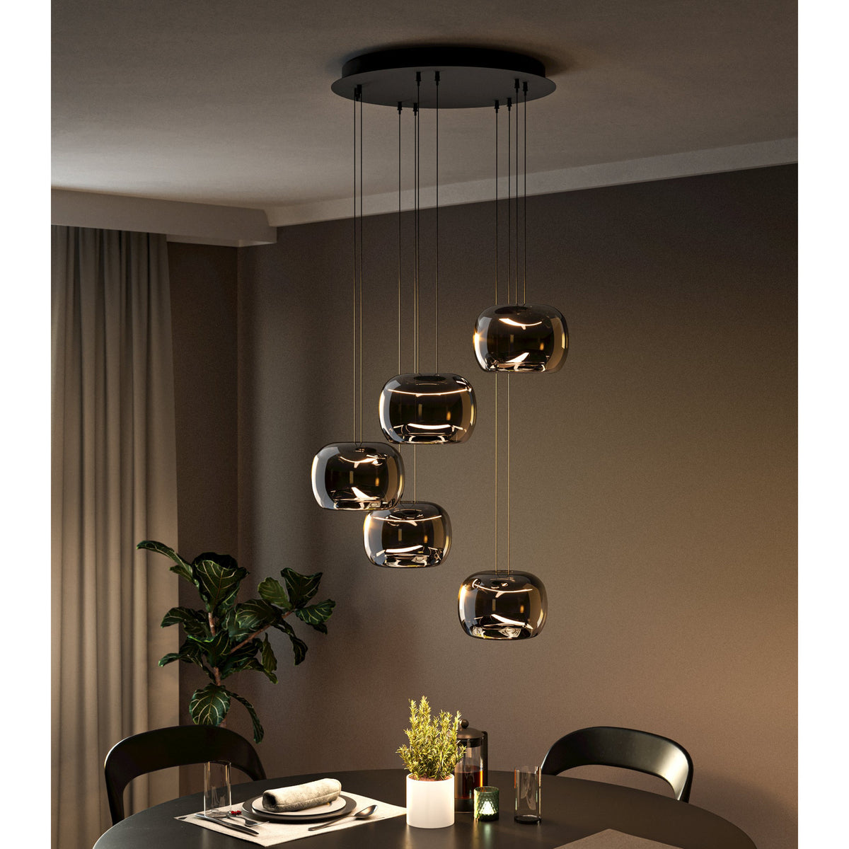 Hortunas 5-light cluster pendant with round black steel ceiling canopy and smoked glass shades staggered on varied cables, shown above a dining table in a dark-toned room.