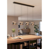 Hortunas linear pendant light with four rounded smoked glass shades on a black steel ceiling bar, shown suspended above a wooden dining table in a living space.