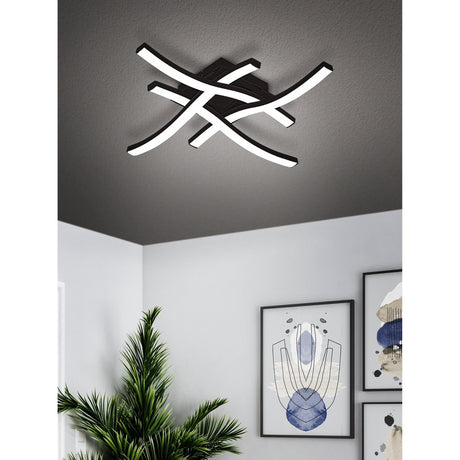 Trosmessa LED 4 Light Flush Ceiling Light in black with four crossing curved arms and white LED strips, shown mounted on a textured grey ceiling above a modern hallway.