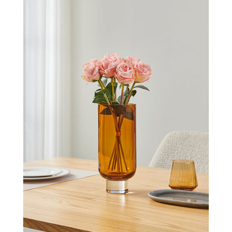 Tudiya Glass Vase 28cm in amber, a tall cylindrical glass vase with a clear glass foot, holding pink roses on a wooden table in a living room setting.