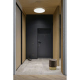 Mantra Tulum CCT dimmable LED flush ceiling light in white with crystalline centre, mounted on a wood-clad ceiling above a dark hallway with a velvet pouffe.