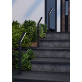 Ugento LED bollard lights in matte black with angled heads and white diffusers, shown lining stone steps beside greenery at a house entrance.
